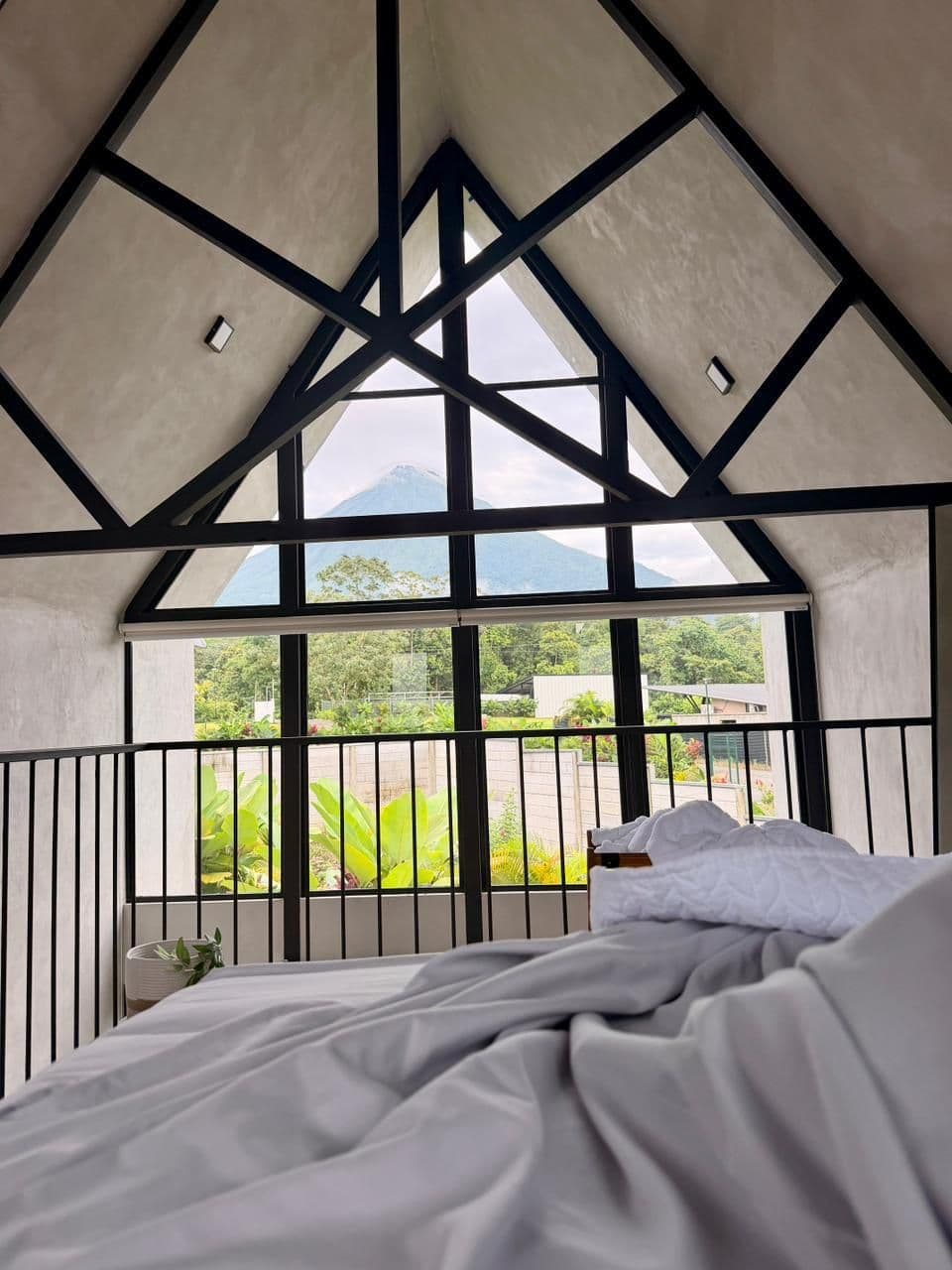 La cama de una villa frente al ventanal, con el Volcán Arenal al fondo
