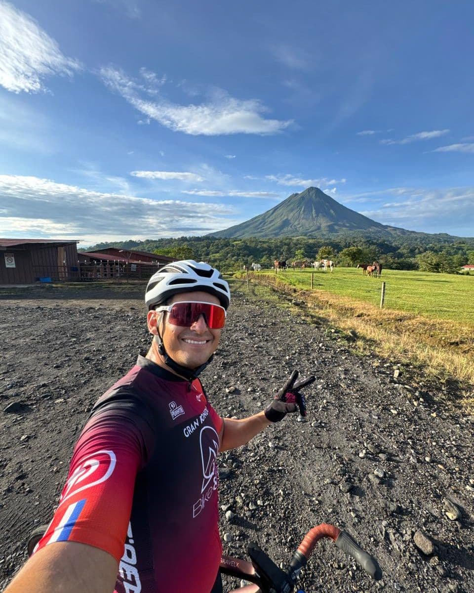 Tony Alvarado en bicicleta sobre un camino de lastre, con el Volcán Arenal al fondo